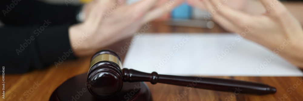 Judges gavel lying on wooden table in courthouse closeup. Male and female hands are gesturing in background. Pretrial settlement of conflicts concept.