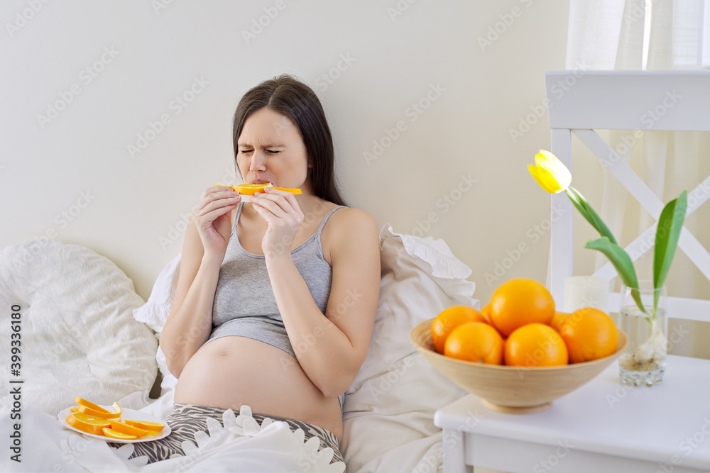 Young beautiful pregnant woman eating oranges sitting in bed at home Young beautiful pregnant woman eating oranges sitting in bed at home