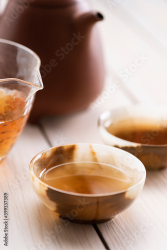 Healthy beverage close up. Chinese old shen puerh tea made in clay teapot and served in glass chahai and  cups of onyx stone on white wooden table
