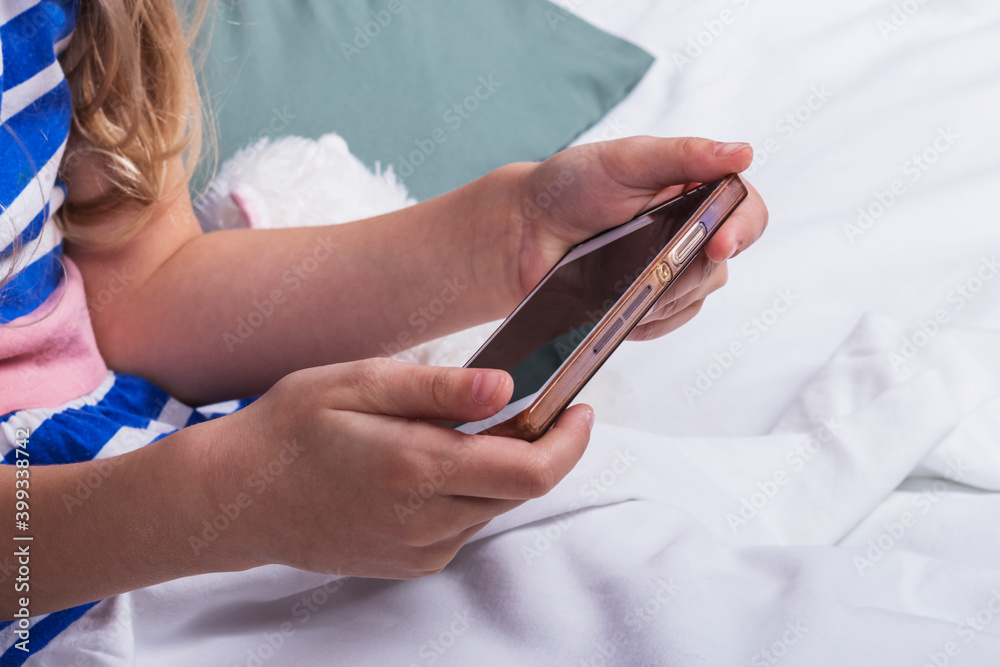 Studio lighting. child, girl with white hair in the hands of the phone. She is in bed. Close-up.
