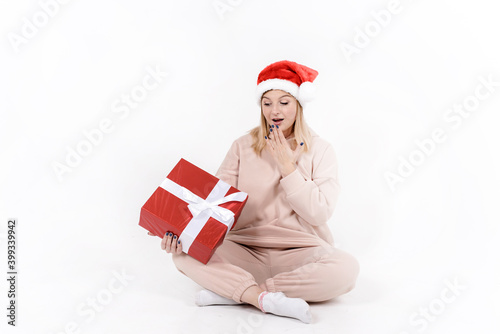 Beautiful young woman holding red Christmas box with white bow sitting on the floor over white background