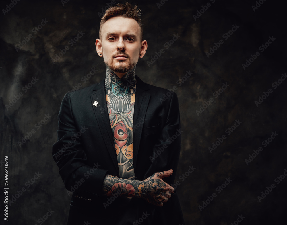 Portrait of a hipster person with tattooed body dressed in luxurious black jacket poses in dark background looking at camera with serious face. Portrait of a hipster person with tattooed body dressed in luxurious black jacket poses in dark background looking at camera with serious face.