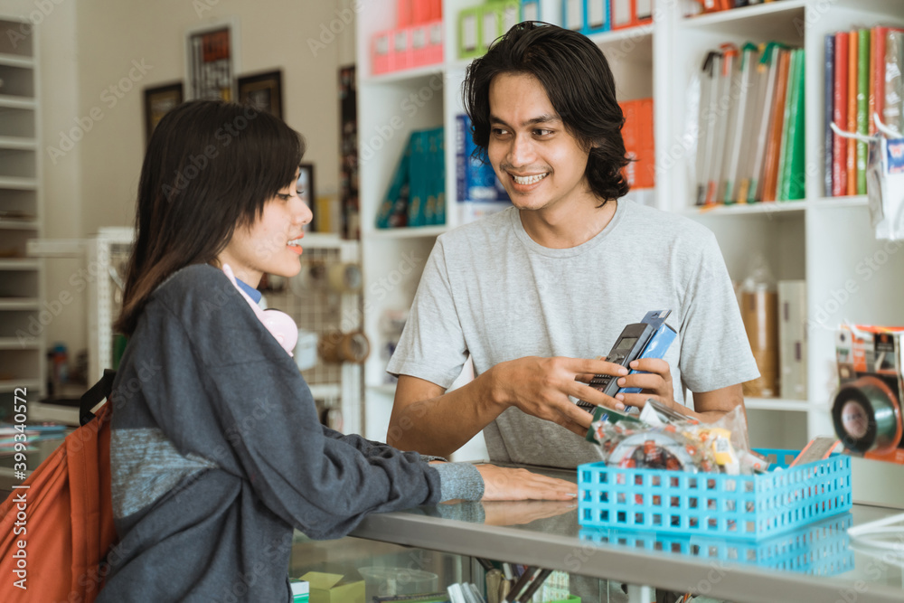 Young girl visiting a stationery shop talks to the male cashier about prices