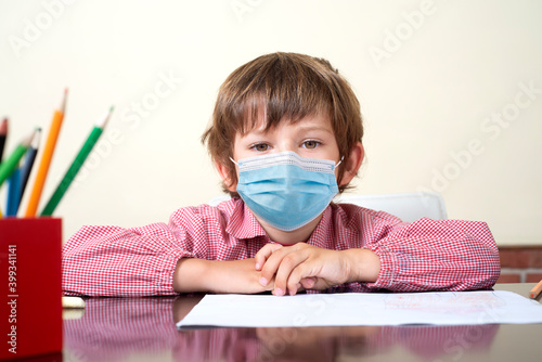 school boy at desk with sanitary mask looks at camera