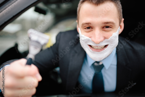 Photography Businessman shaving in car by razor and foam at the wheel
