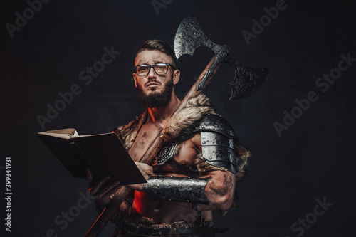 Sad nordic warrior in light armour with fur with eyeglasses and book holding huge axe on his shoulder in dark background.