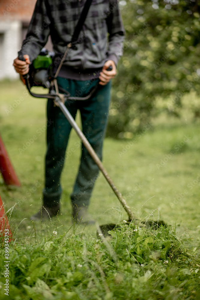 Worker with a gas mower in his hands, mowing grass in front of the house. Trimmer in the hands of a man. Gardener cutting the grass. Lifestyle. Worker with a gas mower in his hands, mowing grass in front of the house. Trimmer in the hands of a man. Gardener cutting the grass. Lifestyle.