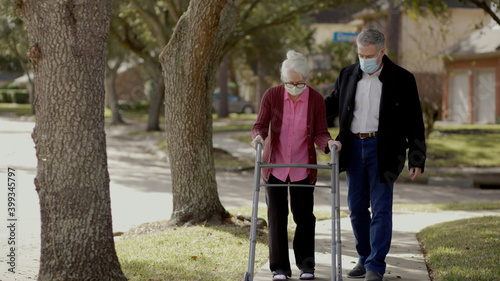 Elderly woman in mask due to the pandemic uses a walker to take a walk outdoors with a friend.