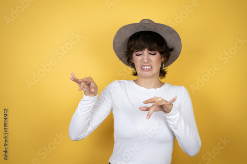 Foto Young caucasian woman wearing hat over isolated yellow background disgusted expression, displeased and fearful doing disgust face because aversion reaction