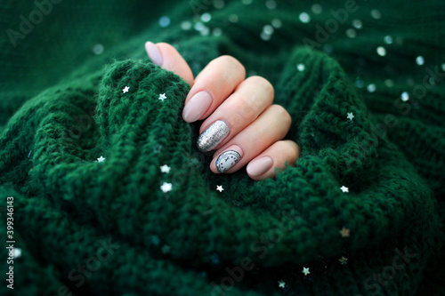 Beautiful female hand in a green sweater with Christmas nail design. Nail design, manicure with chimes pattern. Sequins. Shellac.