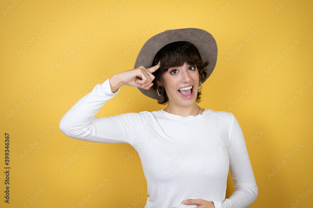 Young caucasian woman wearing hat over isolated yellow background smiling and thinking with her fingers on her head that she has an idea. Young caucasian woman wearing hat over isolated yellow background smiling and thinking with her fingers on her head that she has an idea.