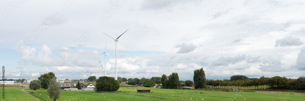 Panorama of windturbines in a Dutch polderlandscape with farms grassland and trees underneath a cloudy sky