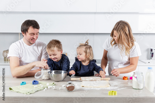 Happy young family with two small children cheerfully prepares dough cookies in the kitchen. Love and tenderness in a relationship.