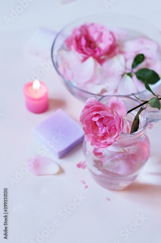 Fresh pink roses, water, petals, candles on a light background, body care products, natural home cosmetics, healthy lifestyle, alternative medicine © Tetiana