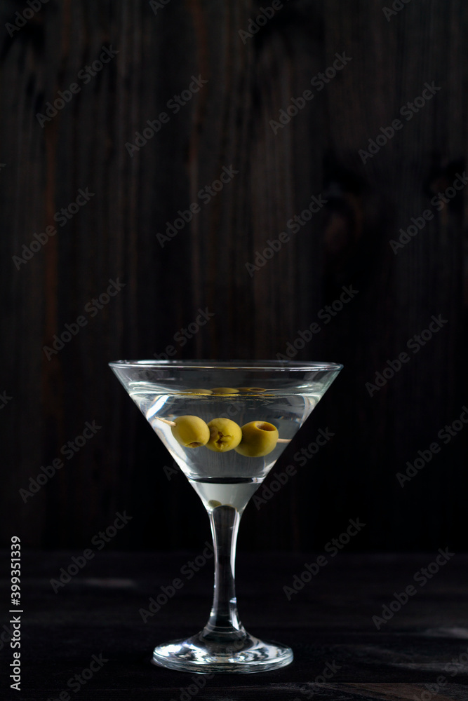Martini glass with cocktail and olives on black background. Cocktail Margarita with olive and ice on the wooden table. copy space. alcohol drinks. vertical Martini glass with cocktail and olives on black background. Cocktail Margarita with olive and ice on the wooden table. copy space. alcohol drinks. vertical
