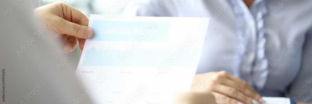 Close up of male hands holding statistics report while lady sitting at the table with clipboard