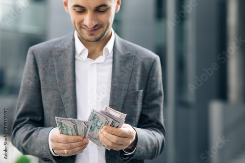 Handsome Rich Man Wearing Stylish Suit Counting Money Standing in the Street Near Office Building photo