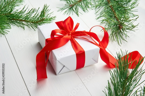 Christmas gift box with red ribbon and pine tree branches on white wooden background