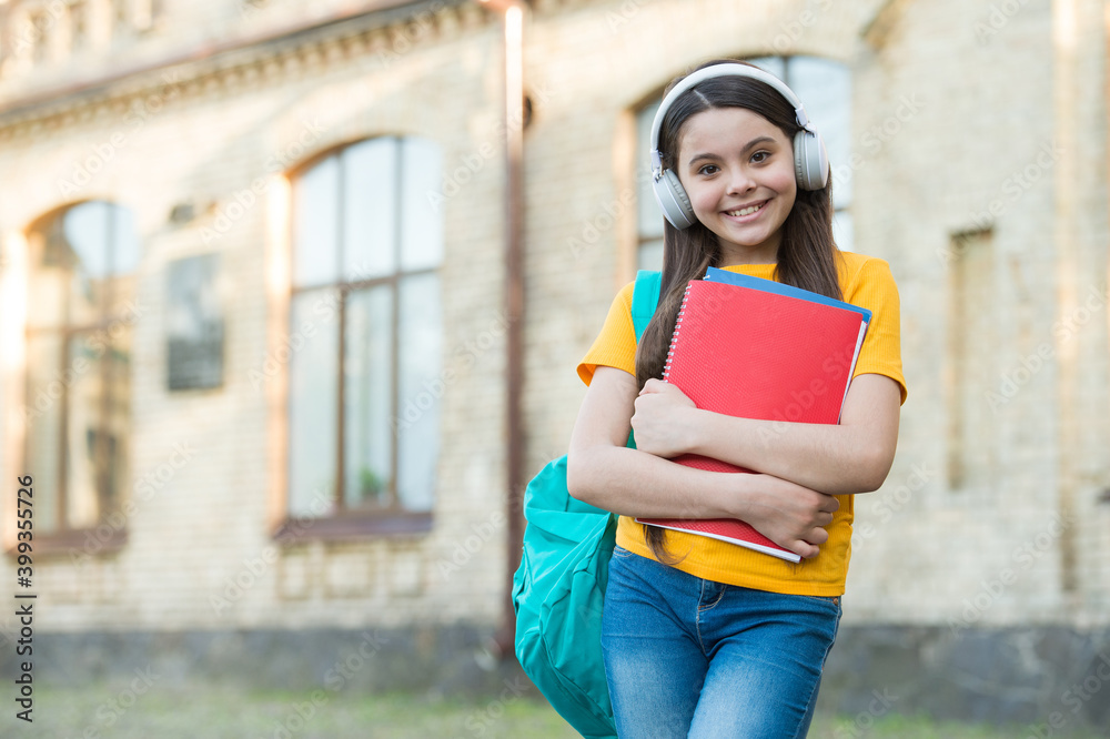 Happy child carry school bag and book wearing modern headphones for listening, copy space Happy child carry school bag and book wearing modern headphones for listening, copy space