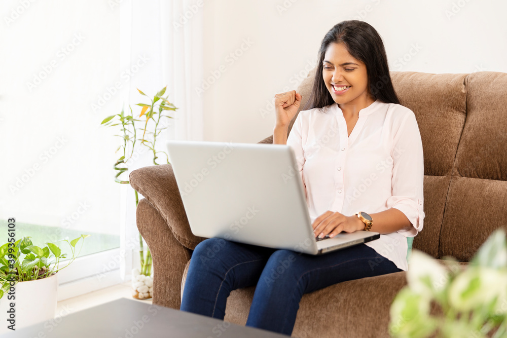 Cheerful pretty young woman working in laptop on sofa at home Cheerful pretty young woman working in laptop on sofa at home
