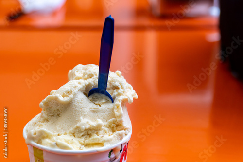 A bucket of vanilla ice cream and a blue spoon.