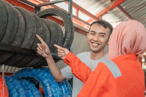 asian male consumer looks at a tire by pointing a finger selecting a tire with a veiled female mechanic in a motorbike workshop © Odua Images