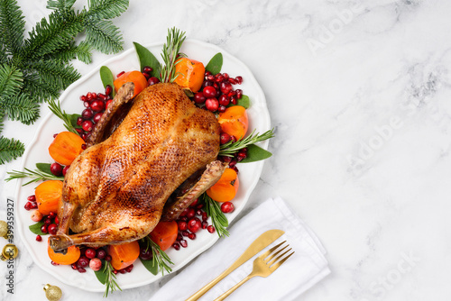 Christmas oven roasted duck on a white plate decorated with cranberries, pomegranate, persimmon, rosemary and sage. Marble background. Copy space. Chrismas food concept. 