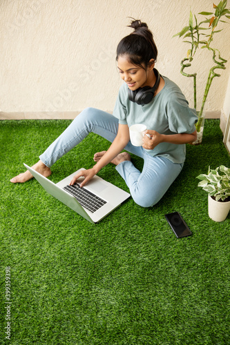 Canvas Print Pretty Young woman working on laptop with coffee cup at balcony artificial grass