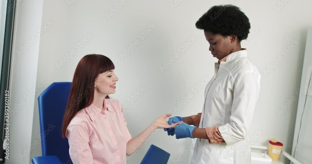Finger blood test. Young female nurse of African American appearance, takes a blood test from a girl of Caucasian nationality. Nurse drawing blood from a woman's hand. HIV medical test, research Finger blood test. Young female nurse of African American appearance, takes a blood test from a girl of Caucasian nationality. Nurse drawing blood from a woman's hand. HIV medical test, research