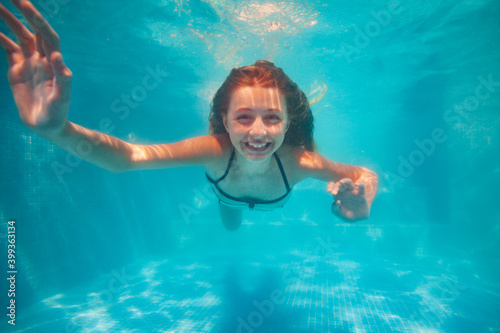 Happy little girl portrait posing underwater gesturing smile in the pool