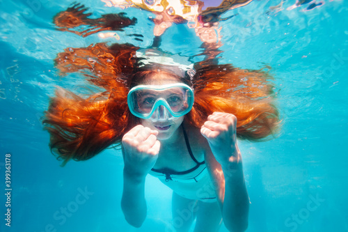 Beautiful underwater portrait of the smiling little girl with long hairs wearing scuba mask show hands gesture