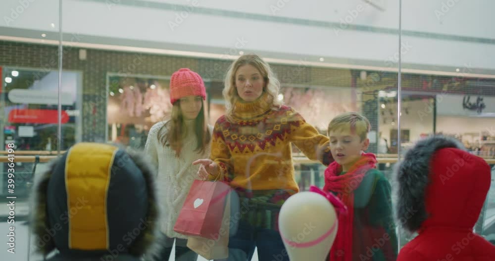 Christmas shopping. Young caucasian pretty mother with two siblings children choosing clothes in store at the shopping mall. Family tradition. Holiday sale. Skating rink. Christmas shopping. Young caucasian pretty mother with two siblings children choosing clothes in store at the shopping mall. Family tradition. Holiday sale. Skating rink.