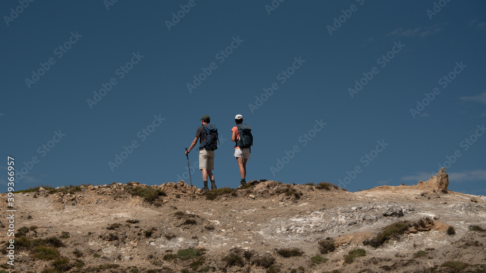 a young woman and a young man standing, side by side, looking at the horizon at the top of a mountain