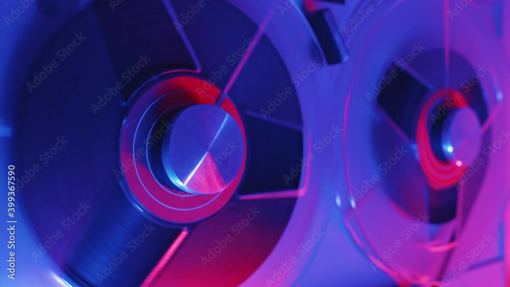 Reel to reel tape recorder playing ultra red blue neon light. Rotating vintage music player close up. Retro tape. Spinning reels metallic color with red disc. Popular Disco Trends 60s, 70s, 80s, 90s. Reel to reel tape recorder playing ultra red blue neon light. Rotating vintage music player close up. Retro tape. Spinning reels metallic color with red disc. Popular Disco Trends 60s, 70s, 80s, 90s.