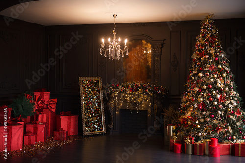 Interior of luxury dark living room with fireplace and chandelier decorated with Christmas tree and gifts photo