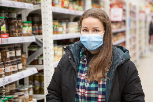 Portrait of a woman in safety mask standing in grocery store wearing warm clothes, Caucasian female looking at camera
