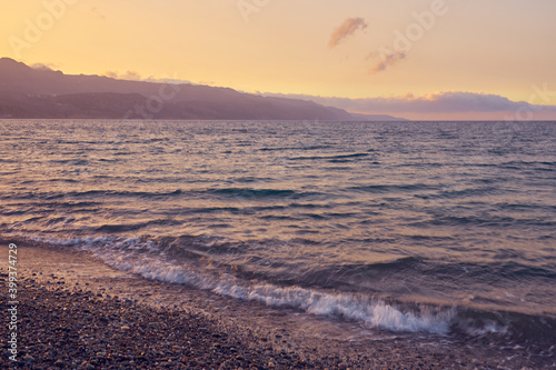 Waves on the pebble shore of the sea at sunset in Crete in Greece.