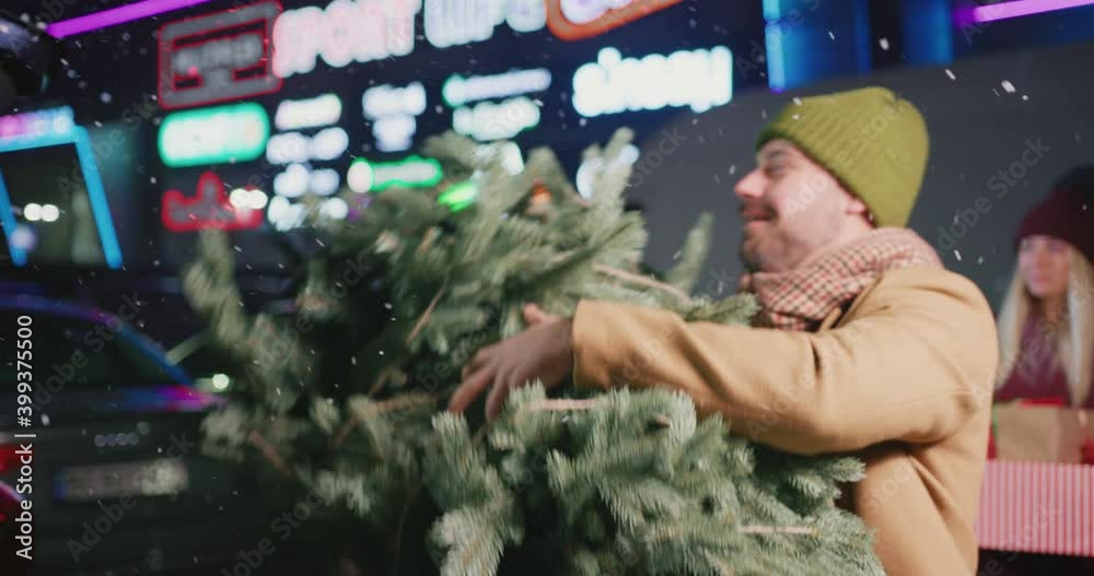 Couple of men putting Christmas tree into back of car. Happy multi-racial millennial friends gathering to spend New Year holidays together. Parking space. Couple of men putting Christmas tree into back of car. Happy multi-racial millennial friends gathering to spend New Year holidays together. Parking space.