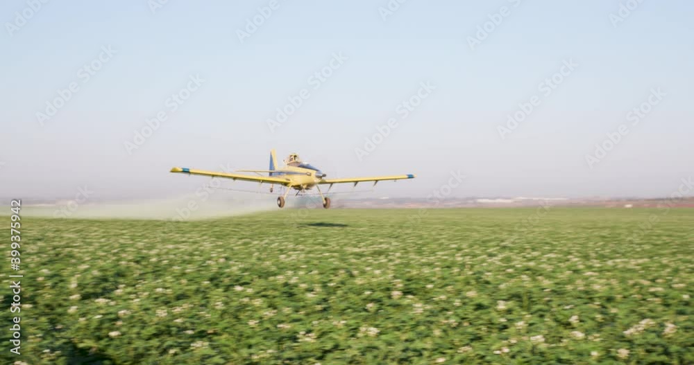 Side view of a crop duster flying low and spraying chemicals over vegetable crops Side view of a crop duster flying low and spraying chemicals over vegetable crops