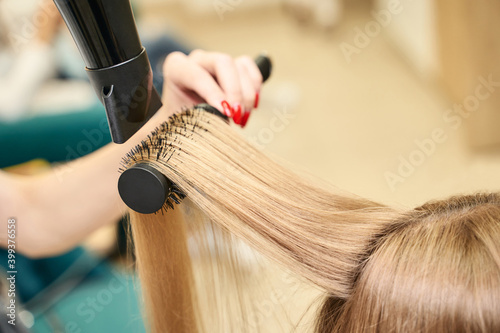 Repair long hair procedure. Haircut at salon. Woman hairstyle. Master hand with brush and fan. Adult female person. Closeup view. Studio equipment. Lady preparation. Blonde dry.