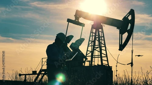 Engineer with laptop walking about oil pumpjack, drone flying