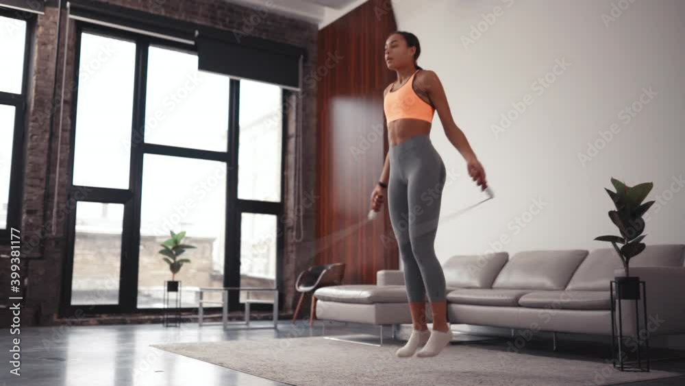 Athletic African American beautiful woman jumping rope as part of her fitness workout in a cozy home environment. Athletic African American beautiful woman jumping rope as part of her fitness workout in a cozy home environment.