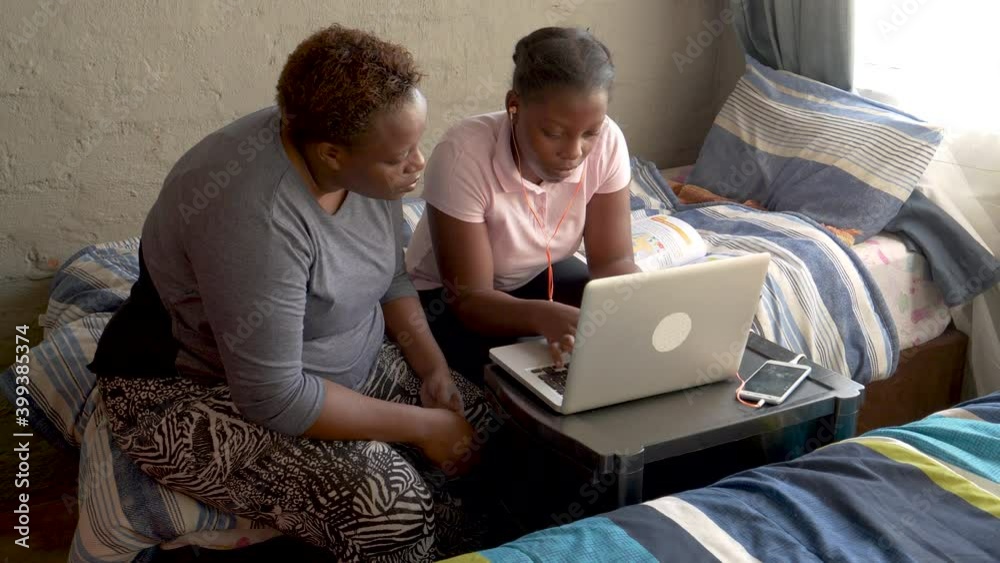 Black African woman home schooling her daughter at home during lockdown for Covid-19 Coronavirus pandemic, South Africa