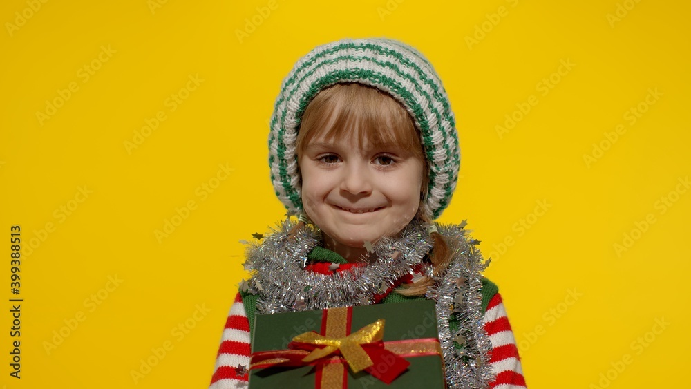 Lovely teen kid girl in Christmas elf Santa helper costume isolated on yellow background. Child giving present gift box to camera, smiling sweetly. People New Year holidays celebration Lovely teen kid girl in Christmas elf Santa helper costume isolated on yellow background. Child giving present gift box to camera, smiling sweetly. People New Year holidays celebration