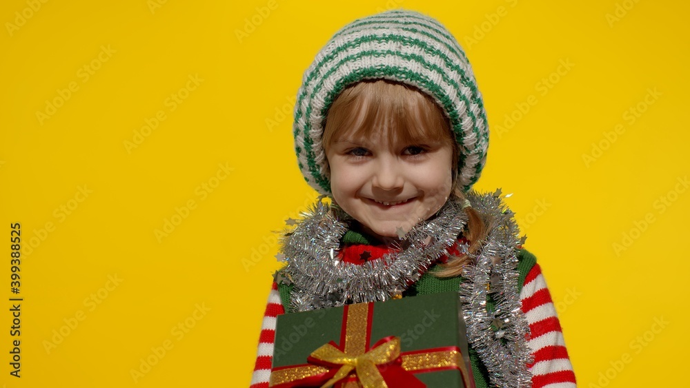 Happy teen kid girl in Christmas elf Santa helper costume isolated on yellow background. Child with present gift box looking to camera, smiling sweetly. People New Year holidays celebration Happy teen kid girl in Christmas elf Santa helper costume isolated on yellow background. Child with present gift box looking to camera, smiling sweetly. People New Year holidays celebration