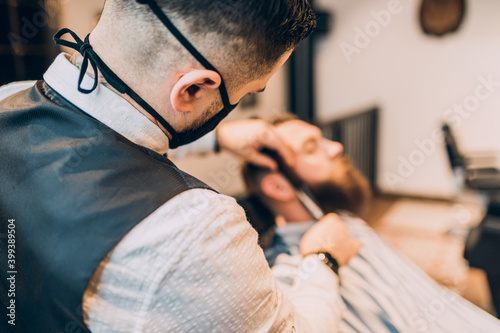 Young good looking hipste man visiting barber shop. Trendy and stylish beard styling and cut.