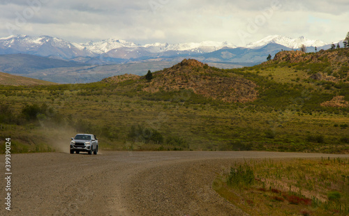 dirt road with pickup truck in the background kicking up dust snowy mountains background