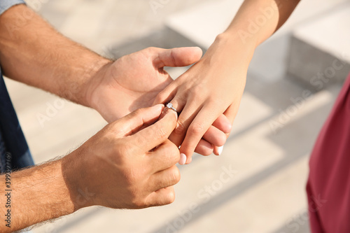 Man putting engagement ring on his girlfriend's finger outdoors, closeup