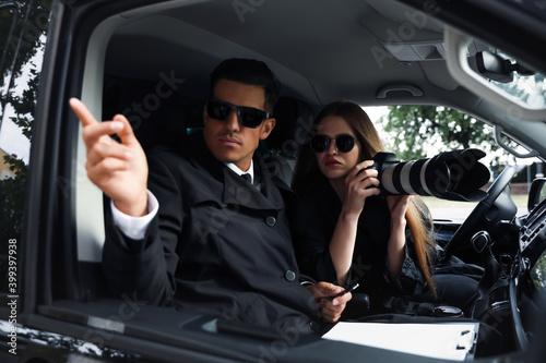 Fotografie Private detectives with modern camera spying from car