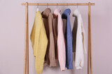 Warm sweaters hanging on wooden rack against pink background